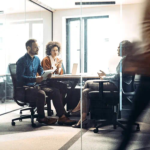 three seated people in glassed office with blurred person walking by