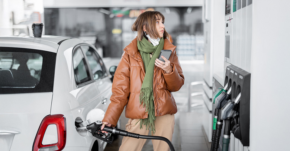 Woman holding a phone and pumping gas at a gas station