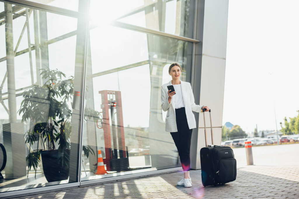 woman outside airport with roller bag and phone