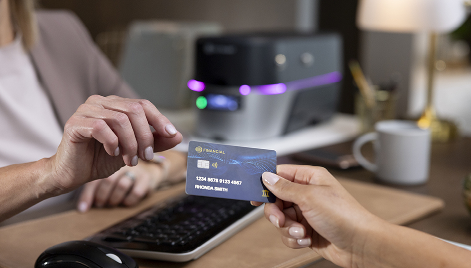 Handing a payment card to a customer service representative at a desk with a card printer in the background
