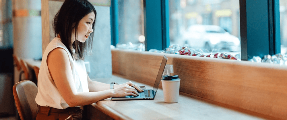 woman with short, dark hair sitting at table and typing on laptop