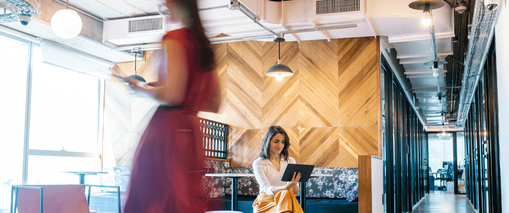 seated woman in lobby area looking at tablet while blurred person passed in front
