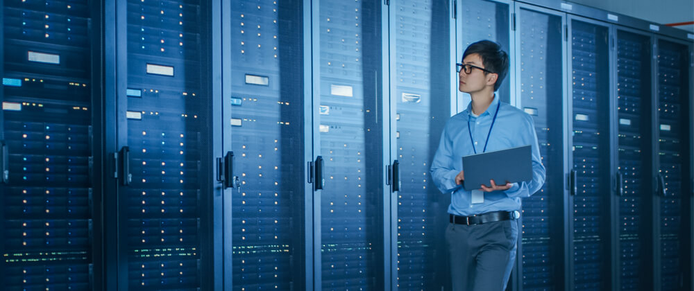 Man walking through a server room holding a laptop